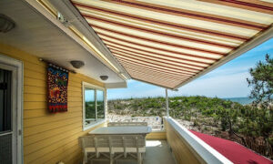 A lakeside summer home with a deck facing the beach and shade provided by a Sunesta Sunplus awning.
